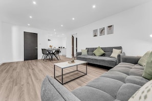 A modern living room with a grey sofa, a coffee table, and a dining area with chairs and a table. - Stylish & Spacious Anfield Flat | WiFi | Sleeps 4 (Anfield)