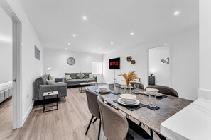 A modern living room with a grey sofa, a dining table set for four, and a flat-screen TV mounted on the wall. - Stylish & Spacious Anfield Flat | WiFi | Sleeps 4 (Anfield)