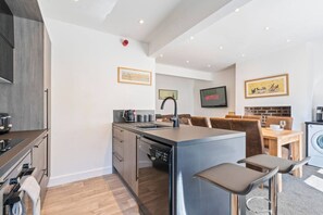 A modern kitchen with a central island, a dining area with a table and chairs, and a living space with a television. - Spacious 5BR House in Staveley | Wi-fi | Sleeps 10 (Staveley)