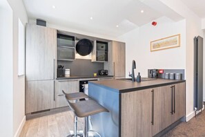 A modern kitchen with a central island, bar stools, and a microwave above the counter. - Spacious 5BR House in Staveley | Wi-fi | Sleeps 10 (Staveley)
