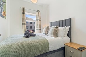 A neatly made bed with a grey headboard, a bedside table with a phone, and a window with curtains. - Spacious 5BR House in Staveley | Wi-fi | Sleeps 10 (Staveley)