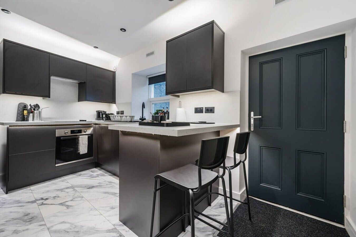 A modern kitchen with dark cabinetry, a marble countertop, and a built-in island with bar stools.