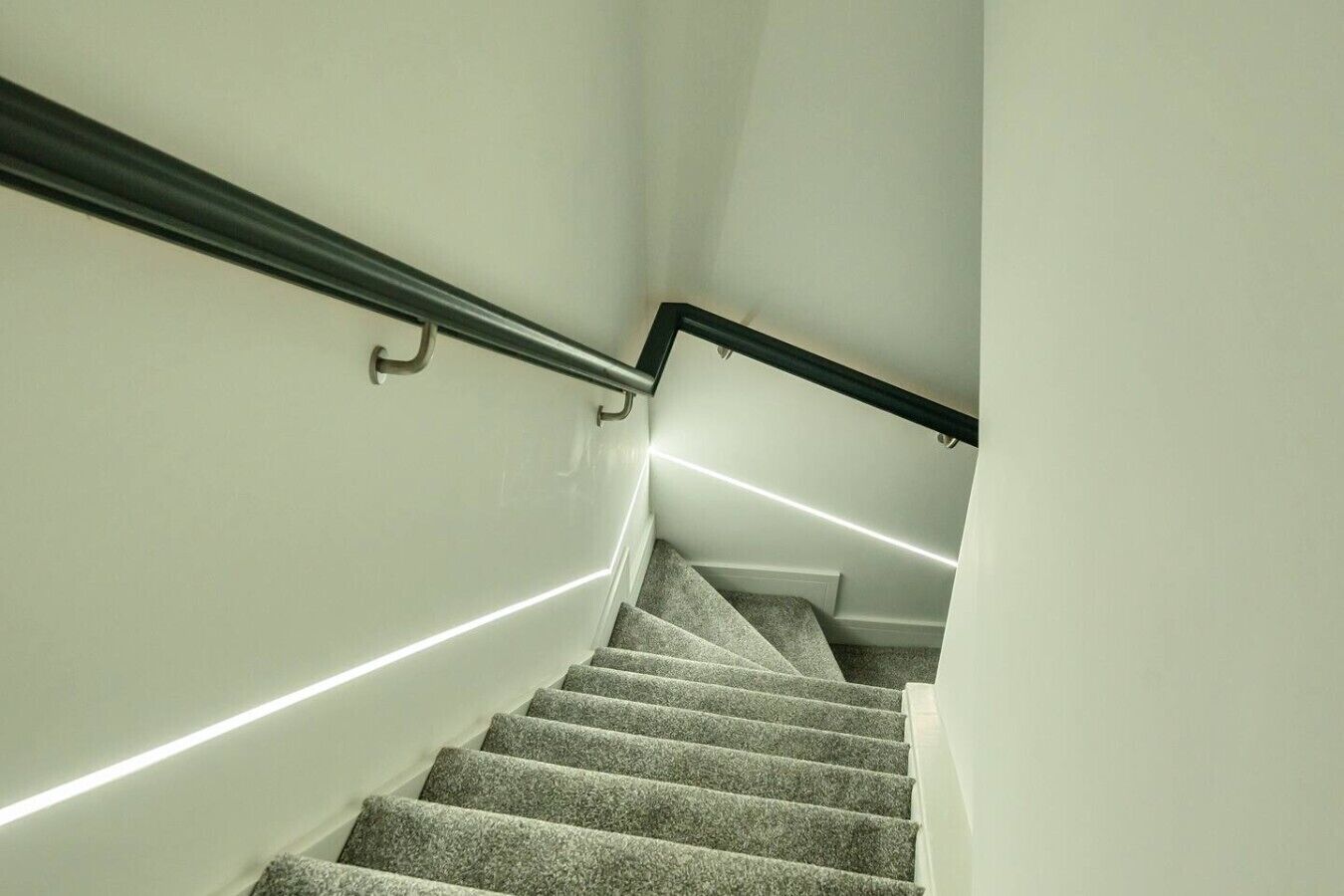 A carpeted staircase with a handrail and a light strip running along the wall.