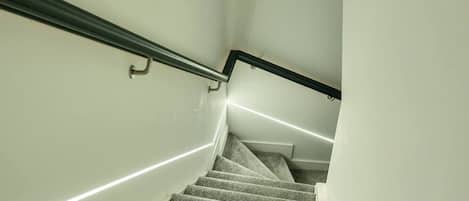 Una escalera alfombrada con barandilla y una franja de luz a lo largo de la pared.