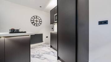 Uma cozinha moderna com armários escuros, piso de mármore e um relógio fixado na parede.