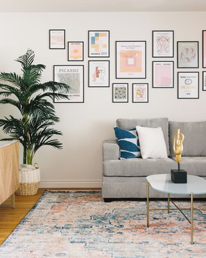 Ein Wohnzimmer mit grauem Sofa, Couchtisch, Topfpflanze und farbenfrohem Teppich.