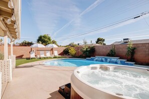 A backyard with a swimming pool, hot tubs, and lounge chairs.