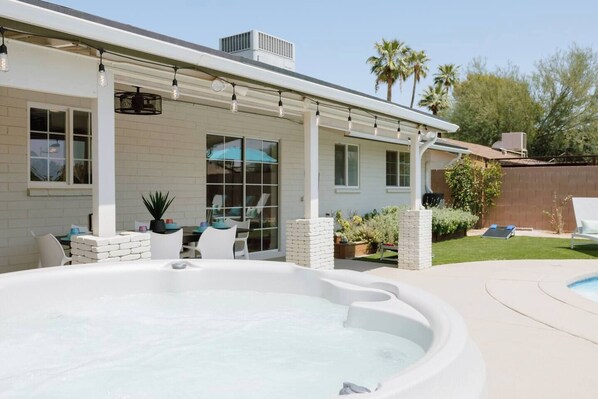 A backyard with a hot tub, outdoor seating, and a pool.