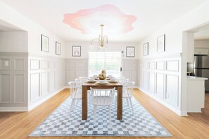 A dining area with a checkered rug, white chairs, a wooden table, and a chandelier. - Muse: Scottsdale Home, Pool & Spa (Scottsdale)