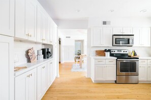 A modern kitchen with white cabinets, a microwave, stove, and a coffee maker.