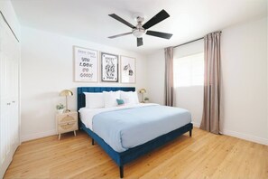 Ein Schlafzimmer mit einem Bett, einem Nachttisch, einem Deckenventilator und einem Fenster mit Vorhängen.