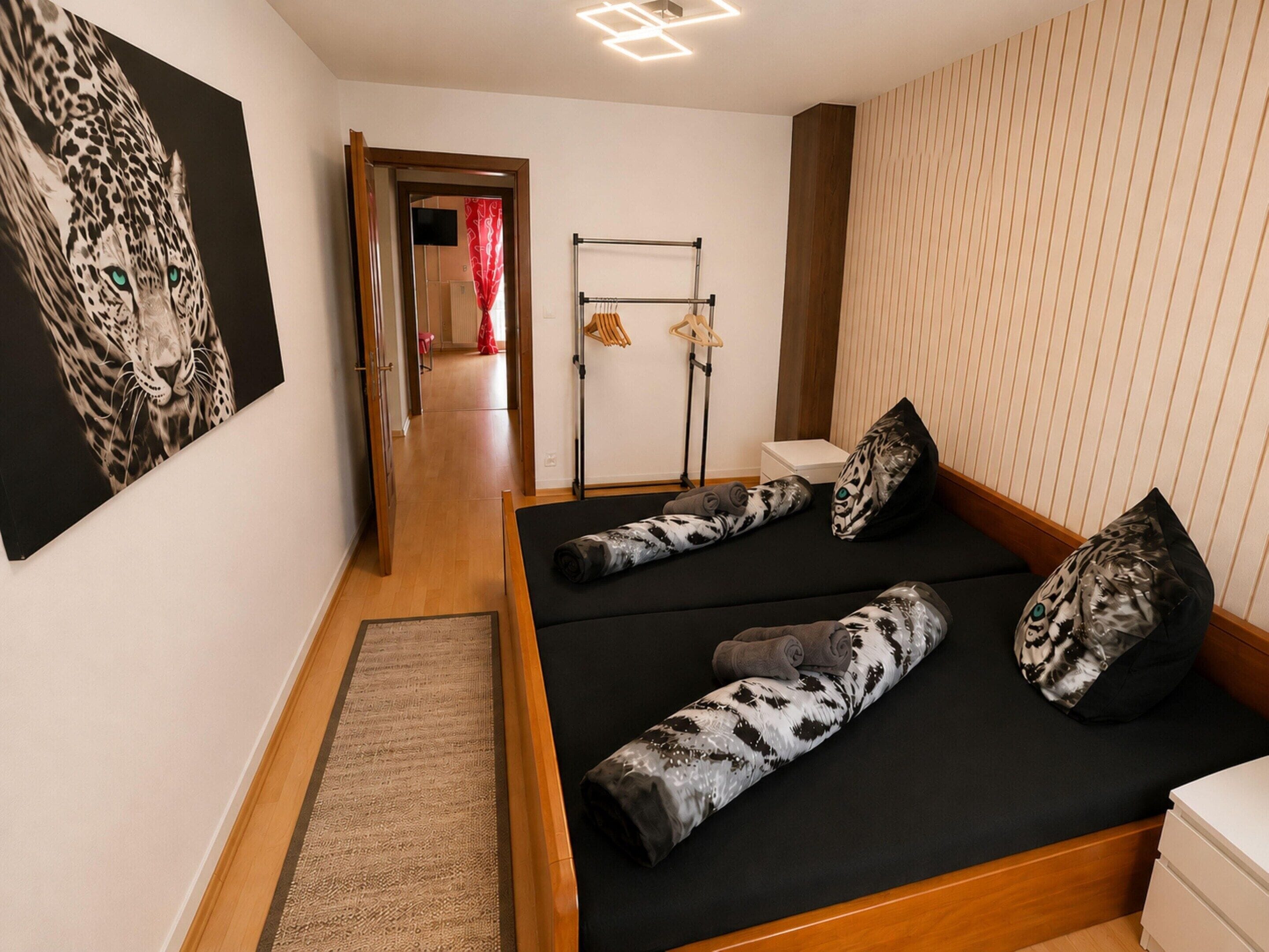 A modern room with a bed, a painting, a wooden floor, and a hallway leading to another room.