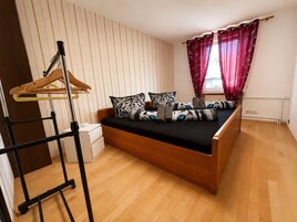 Un dormitorio con una cama de madera, una mesita de noche, un perchero y una ventana con cortinas.