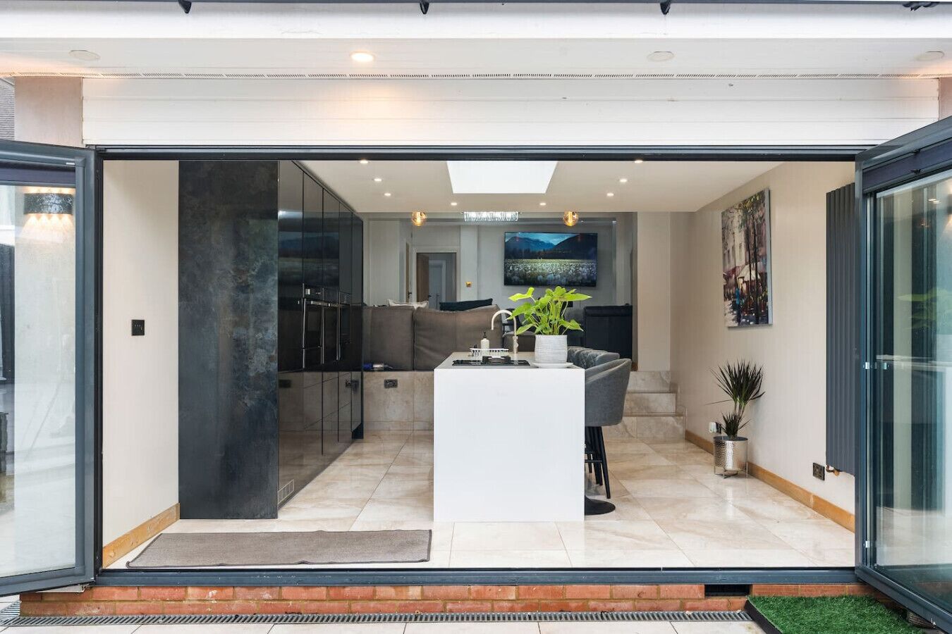 A modern kitchen with a central island, glass doors leading to a dining area, and a view of the cityscape.