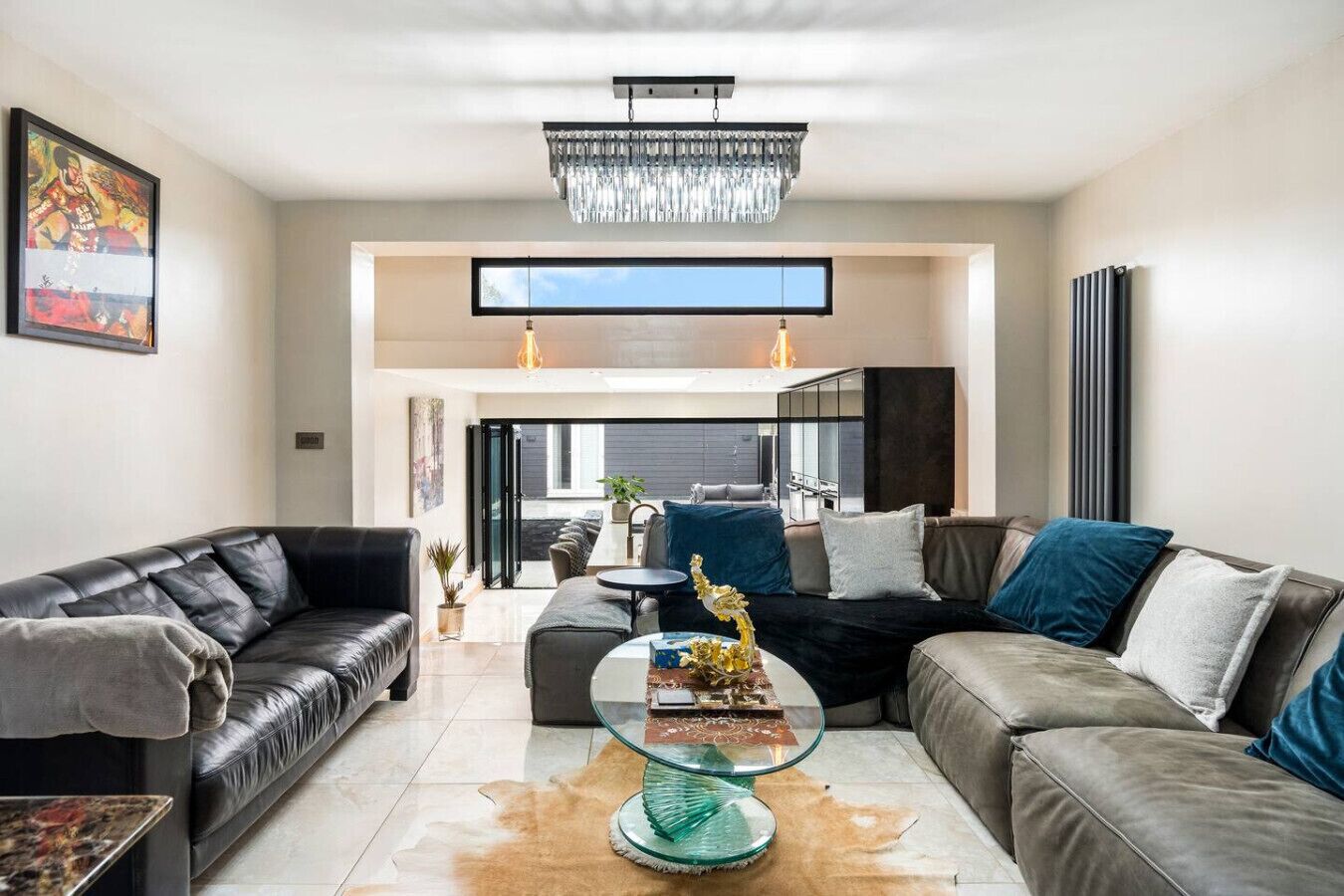 A modern living room with leather sofas, a glass coffee table, and a chandelier.