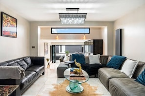A modern living room with leather sofas, a glass coffee table, and a chandelier. - Modern 5 Bedroom House in Hove, Sleeps 8, Van & Car Parking, EV Plug (Brighton and Hove)