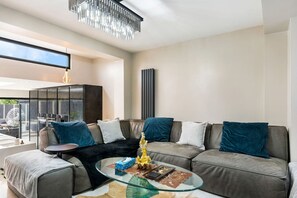 Un salon moderne avec un canapé d’angle, une table basse en verre et une grande fenêtre.