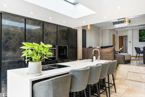 Eine moderne Küche mit einer zentralen Kochinsel, Barhocker und einem Essbereich mit einer Couch und Stühlen.