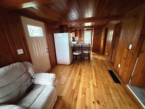 A cabin interior with a wooden floor, a sofa, a refrigerator, and a dining area with chairs. - Driftwood House. Sleeps 4. Beach Access, Parking (Seabrook)