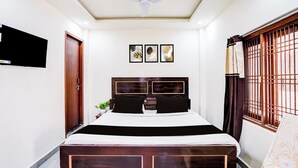 Una camera da letto con un letto, una ventola a soffitto, una TV fissata al muro e una finestra con grate.