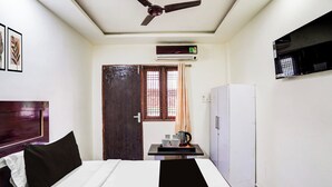 Camera d'albergo con un letto, una ventola a soffitto, un condizionatore, un frigorifero e una finestra con tende.