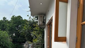 A balcony with a tiled floor, a metal railing, and a view of a street with trees and parked vehicles. - Charming B&B Retreat in the Heart of Cha (Chandigarh)