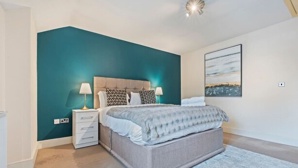 Quarto com cama, mesas de cabeceira, luminária, um quadro na parede e um tapete.