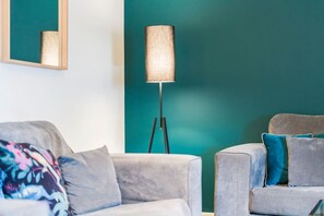 Uma sala de estar moderna com uma parede de destaque verde-água, um abajur e dois sofás cinzas com almofadas.