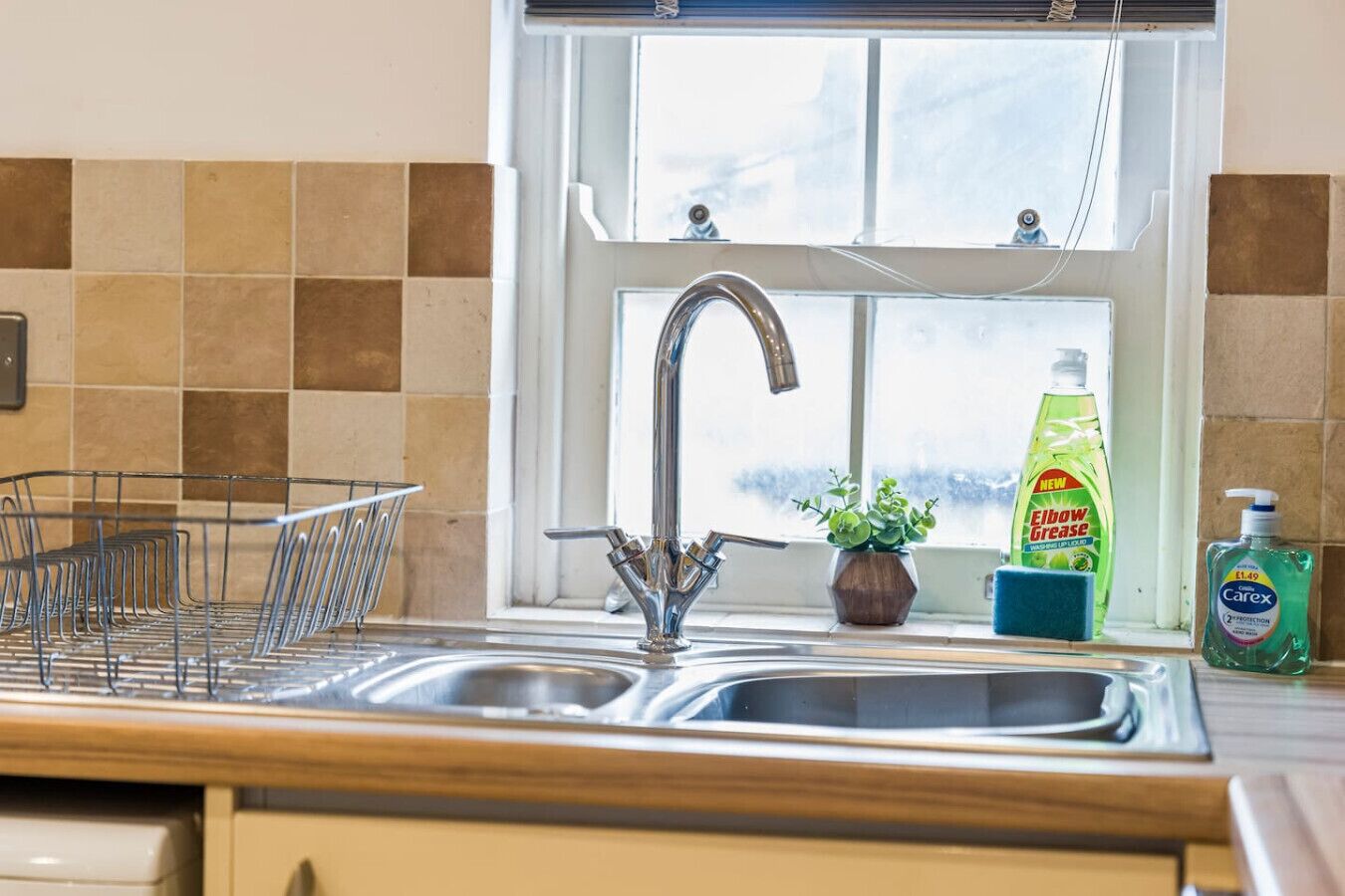 A kitchen with a double sink, a window above the sink, and a plant on the windowsill.