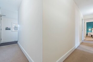 Ein Flur mit Teppichboden, weißen Wänden und einer Tür zu einem Schlafzimmer mit Bett und Nachttisch.