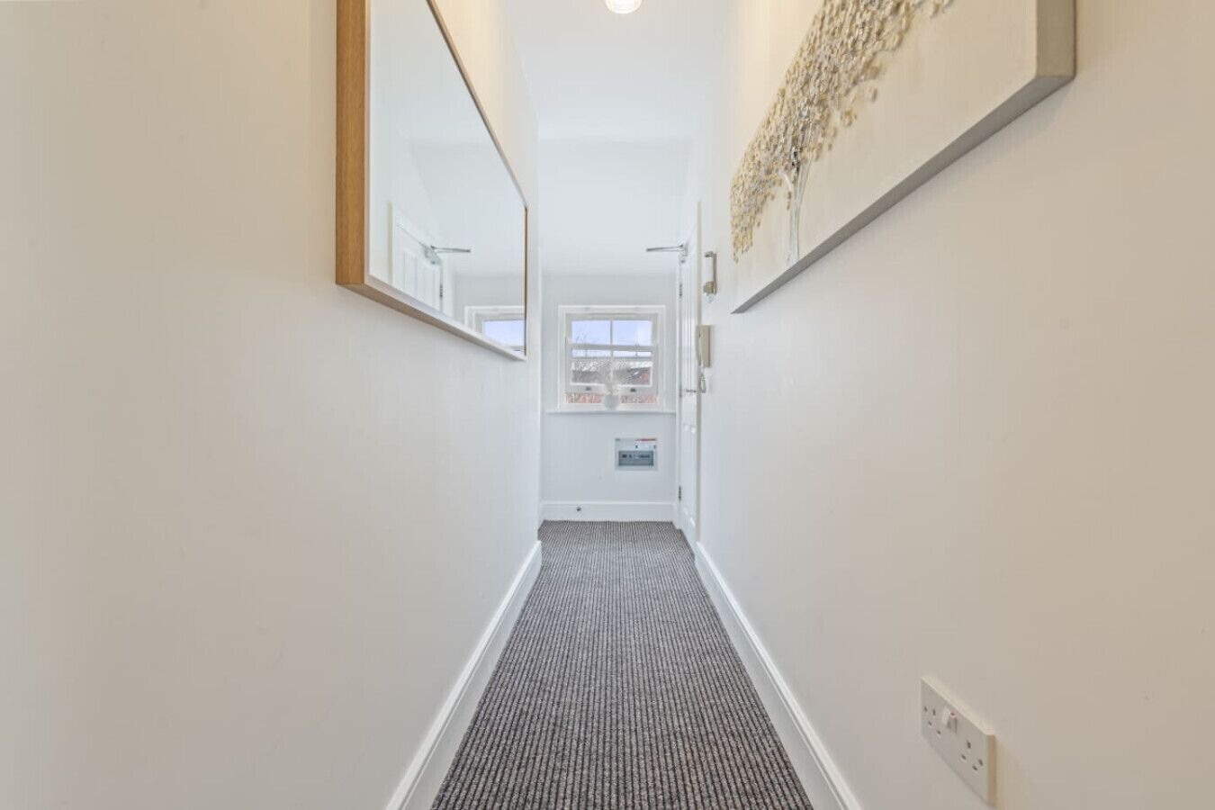 A narrow hallway with a carpeted floor, a door at the end, and a wall-mounted light fixture.