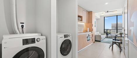A modern laundry room with two front-loading washing machines, a small kitchenette, and a dining area with a view of the city.