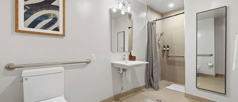 A modern bathroom with a toilet, sink, shower, and a large mirror.