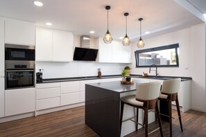 A modern kitchen with white cabinets, a black island, and pendant lighting. - Luxury Villa with Private Pool Near Faro Beach, Offering Unparalleled Comfort! (Faro)