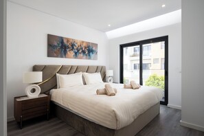 A modern bedroom with a large bed, two bedside tables, a painting on the wall, and a view through a large window. - Luxury Villa with Private Pool Near Faro Beach, Offering Unparalleled Comfort! (Faro)