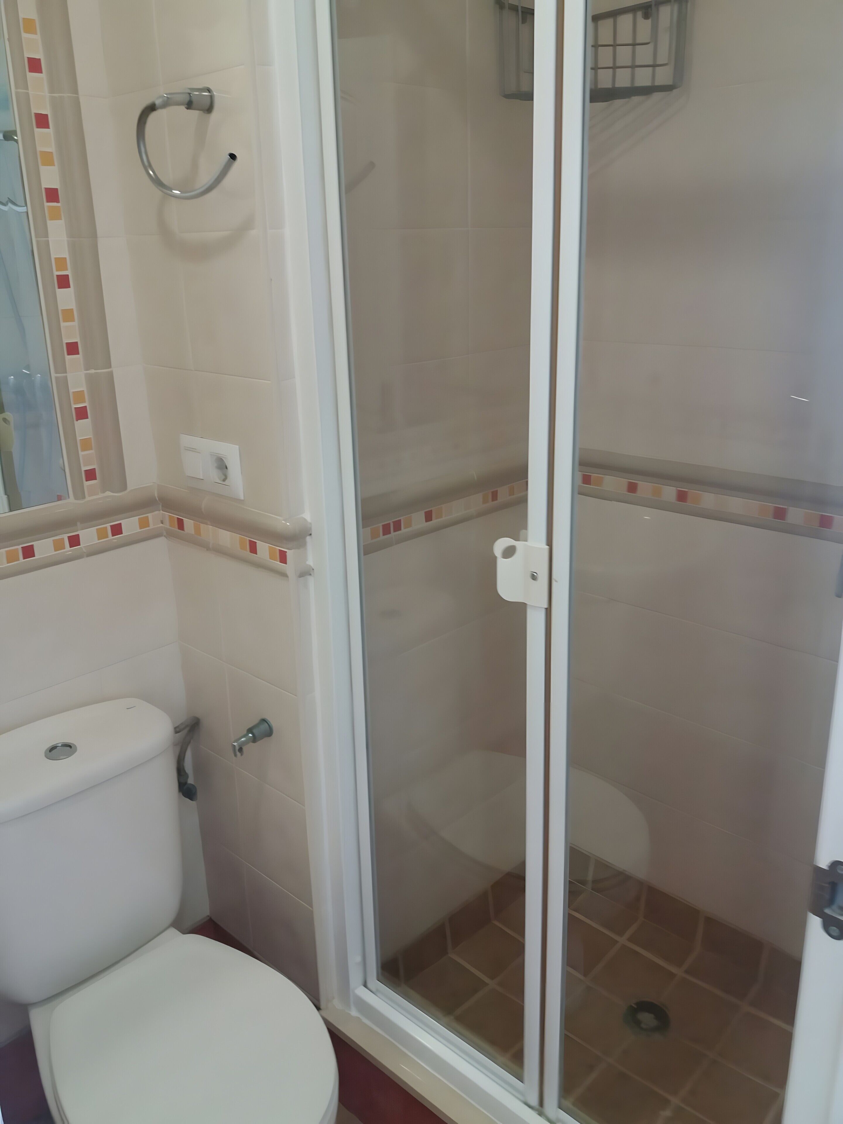 Un baño con inodoro, cabina de ducha y pared de azulejos con un detalle decorativo.