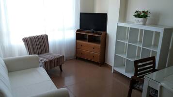 Un salon comprenant un canapé, un fauteuil à rayures, un meuble pour la télévision, un buffet en bois et une table en verre.