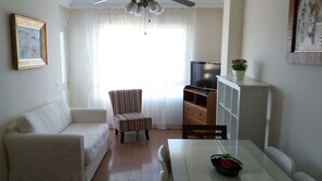 Una sala de estar con un sofá, un sillón a rayas, un mueble para televisión y una mesa de comedor con un cuenco de fruta.