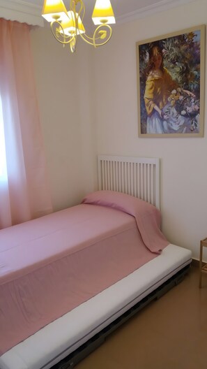 Un dormitorio con cama, un radiador, un cuadro en la pared y una ventana con cortinas.