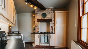 A kitchen with a stone wall, wooden cabinets, a stove, and a window.