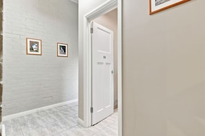 A hallway with a white brick wall, two framed pictures, a white door, and a tiled floor. - Edinburgh Historic Twin Room (Hobart)