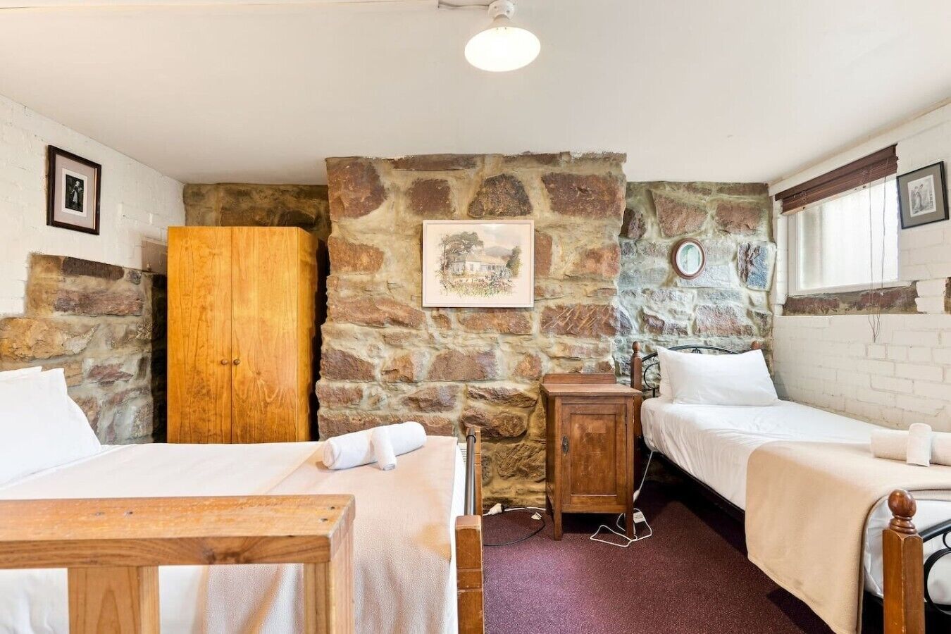 Ein Zimmer mit zwei Betten, einem Holzschrank, einer Steinsäule und einem gerahmten Bild.