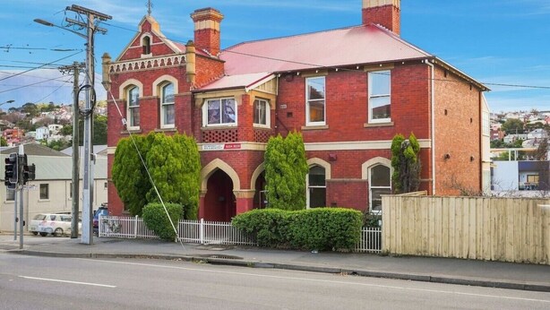 A red brick building with a prominent arched entrance, a large window, and a chimney. - Edinburgh Single Room (Hobart)