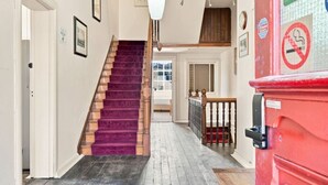 A hallway with a wooden staircase, a red trash bin, and a view to another room. - Edinburgh Single Room (Hobart)