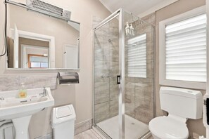 Ein modernes Badezimmer mit einer Duschkabine, einer Toilette, einem Waschbecken mit Seifenspender und einem Handtuchhalter.