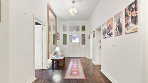 A hallway with wooden flooring, a red patterned rug, a table with a lamp, and wall-mounted artwork. - Edinburgh Single Room (Hobart)