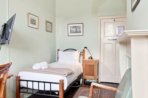 Ein Schlafzimmer mit einem Bett, einem Nachttisch, einer Lampe und einem an der Wand befestigten Fernseher.