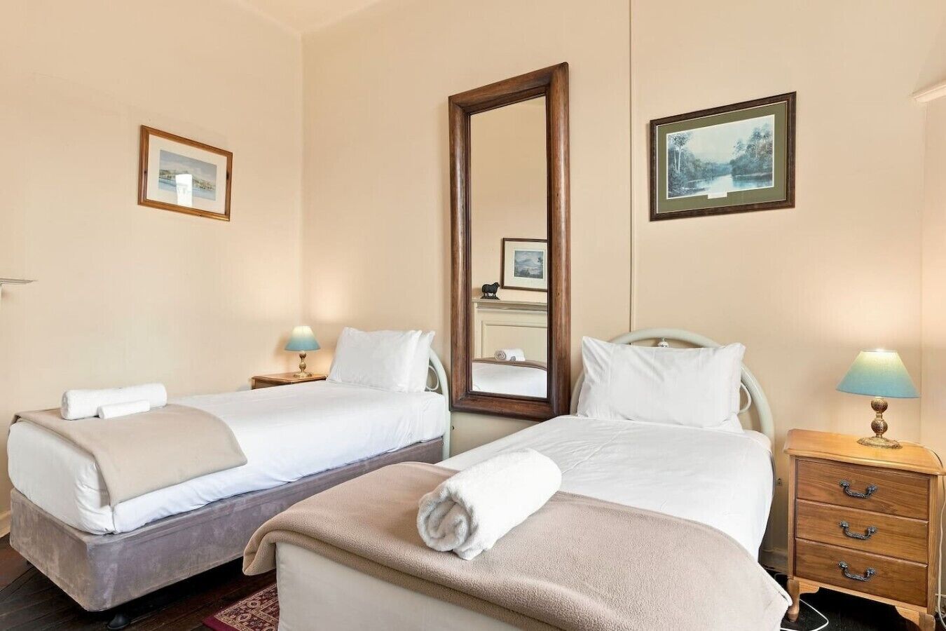 Une chambre d’hôtel avec deux lits, un grand miroir, des tables de chevet avec des lampes et des tableaux encadrés aux murs.