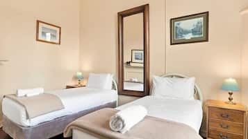 Habitación de hotel con dos camas, un espejo grande, mesitas de noche con lámparas y cuadros en las paredes.