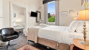 Une chambre d’hôtel comprenant un lit, un bureau, une chaise, une télévision, une fenêtre avec des rideaux et une lampe.